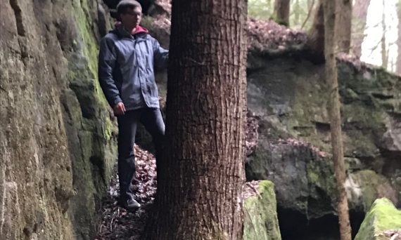 man stands next to hemlock tree growing in rocks